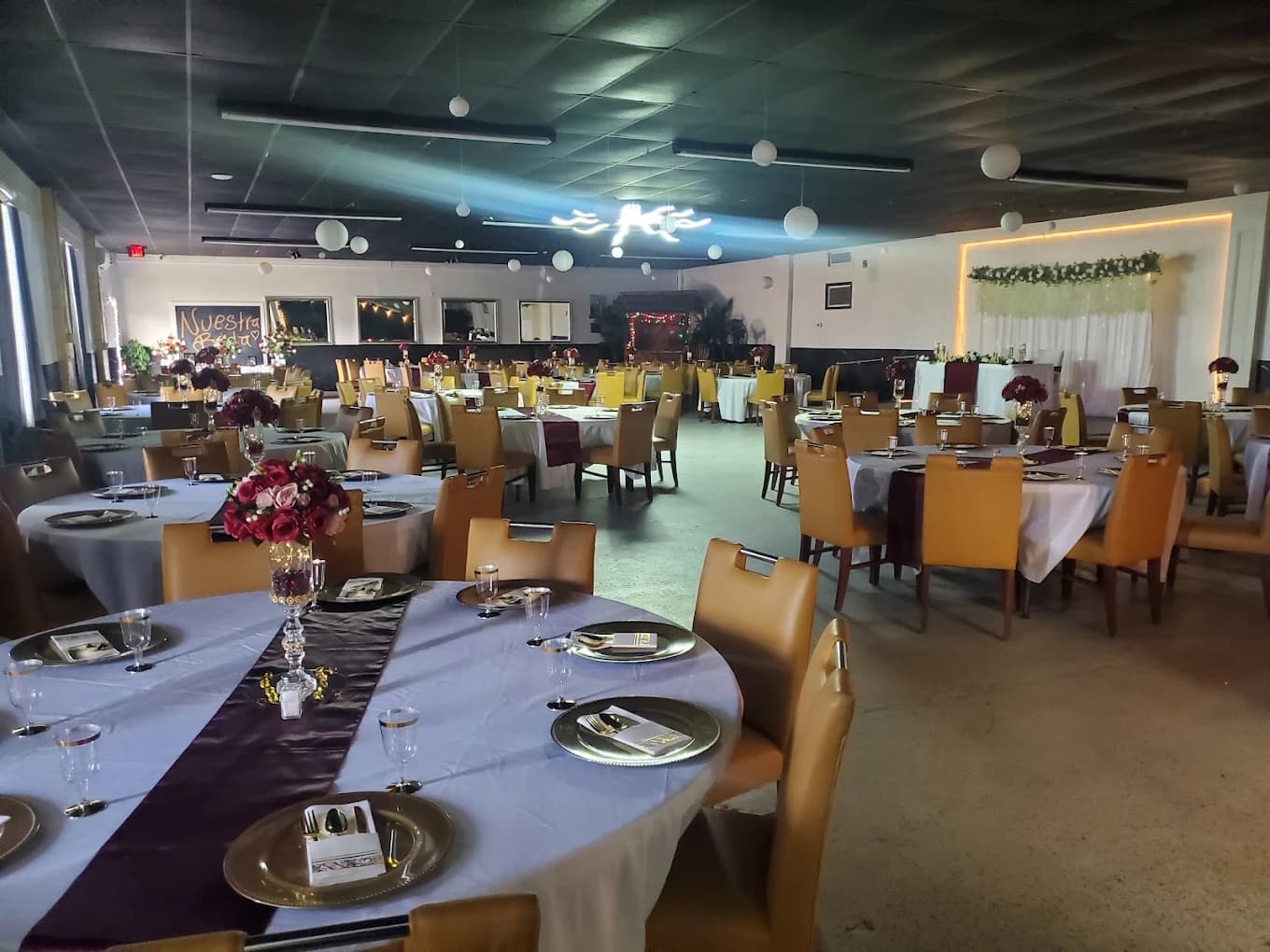 The main hall at Bluebird Event Center set for a formal reception, with round tables in white and burgundy linen, gold chargers and floral centrepieces